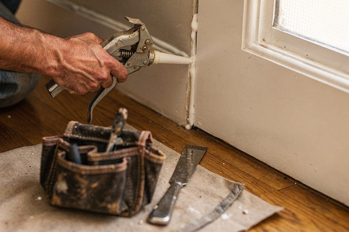 Hand applying caulk along a doorframe seam during a repair call